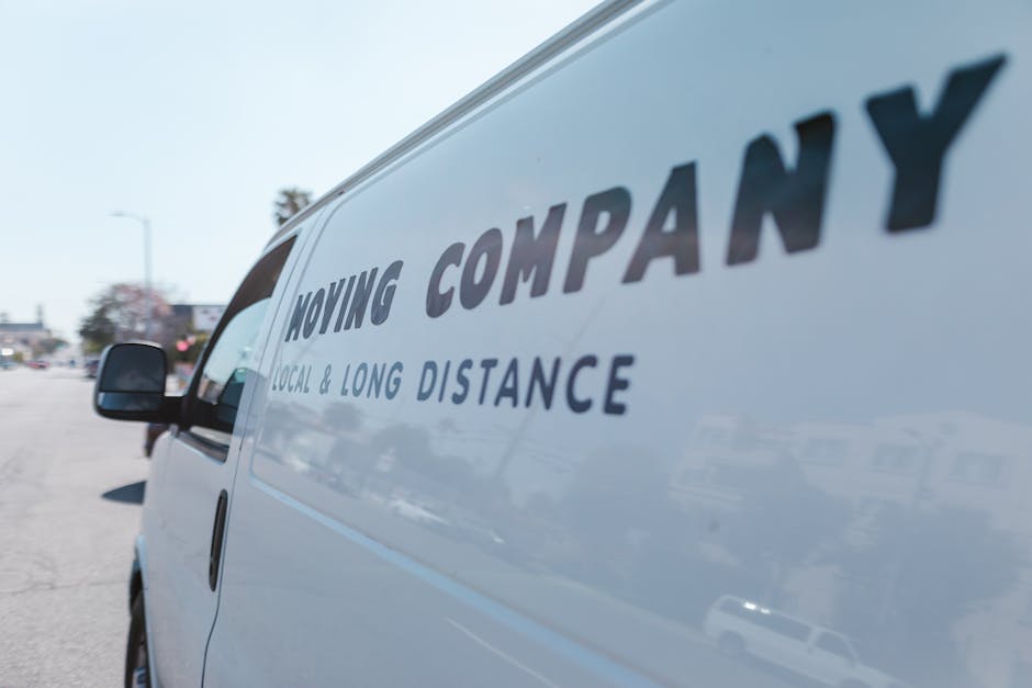 Close-up view of the side of a white moving van parked outside, displaying the company's logo and text that reads 'Moving Company', along with the description 'Local & Long Distance' in blue lettering